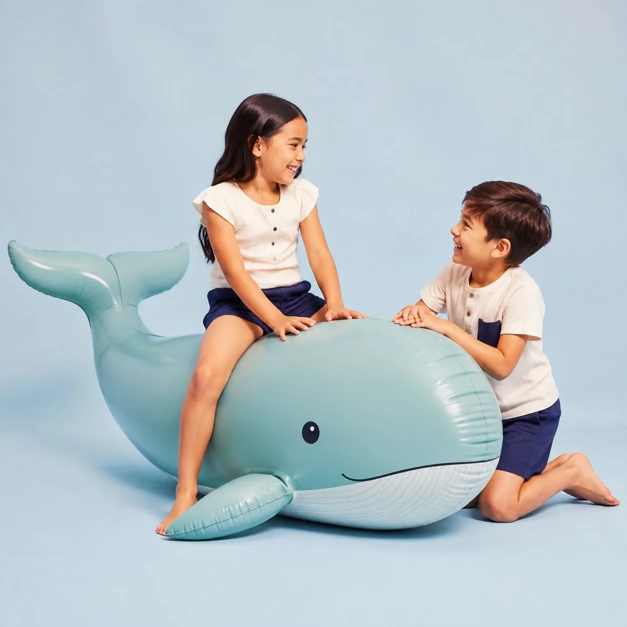 Two children playing together on a teal whale inflatable